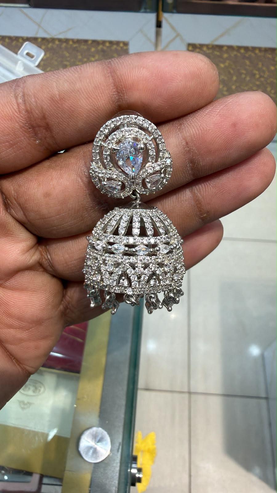 Silver AD Jhumka earring held in hand showing full CZ pavé dome body with pear-cut stud top, leaf-shaped side stones and crystal drops at base