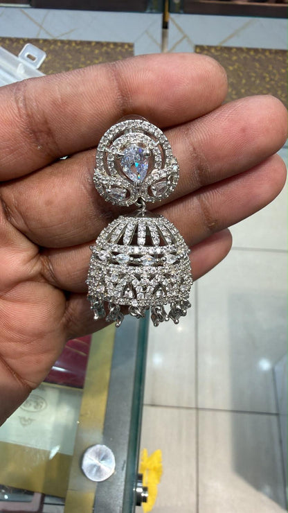 Silver AD Jhumka earring held in hand showing full CZ pavé dome body with pear-cut stud top, leaf-shaped side stones and crystal drops at base