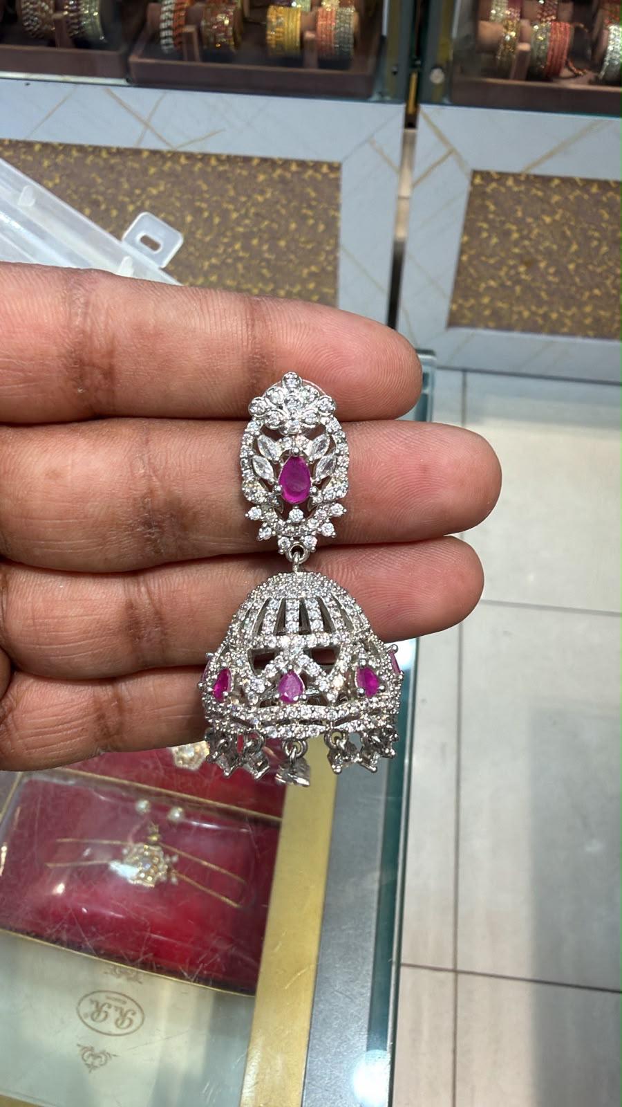 Silver AD Jhumka earring with ruby accents held in hand showing CZ pavé dome body, oval ruby stud top with leaf stones and crystal drops at base