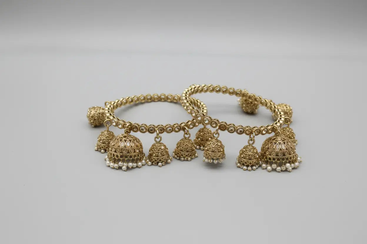 Decorative gold bangles with 5 hanging jumki charms on a white fabric background