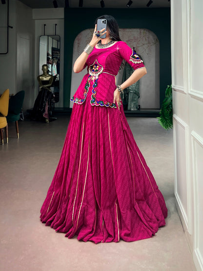 Front view of model in rani pink lehenga choli showing full peplum blouse with Kutchi medallion patch and cowrie shell tassels