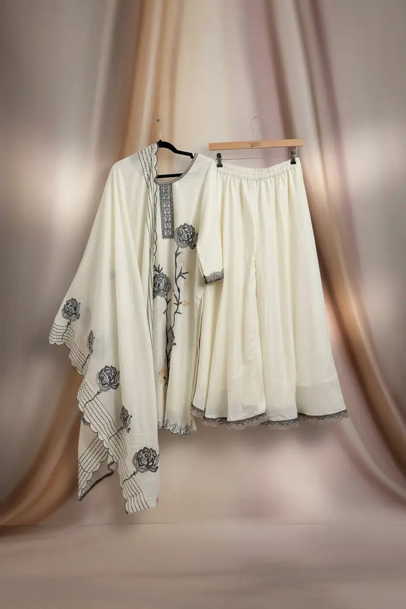 White embroidered outfit with a matching skirt hanging on a wooden hanger against a white wall.