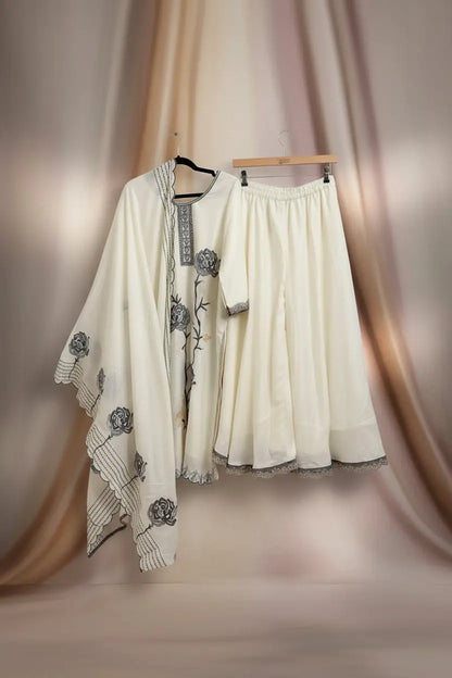 White embroidered outfit with a matching skirt hanging on a wooden hanger against a white wall.