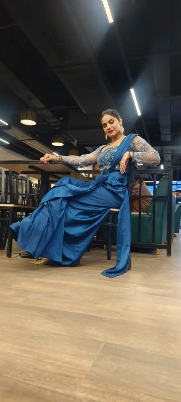 dhoti saree with heavy blouse fully sequins Woman in a blue saree sitting on a chair indoors.