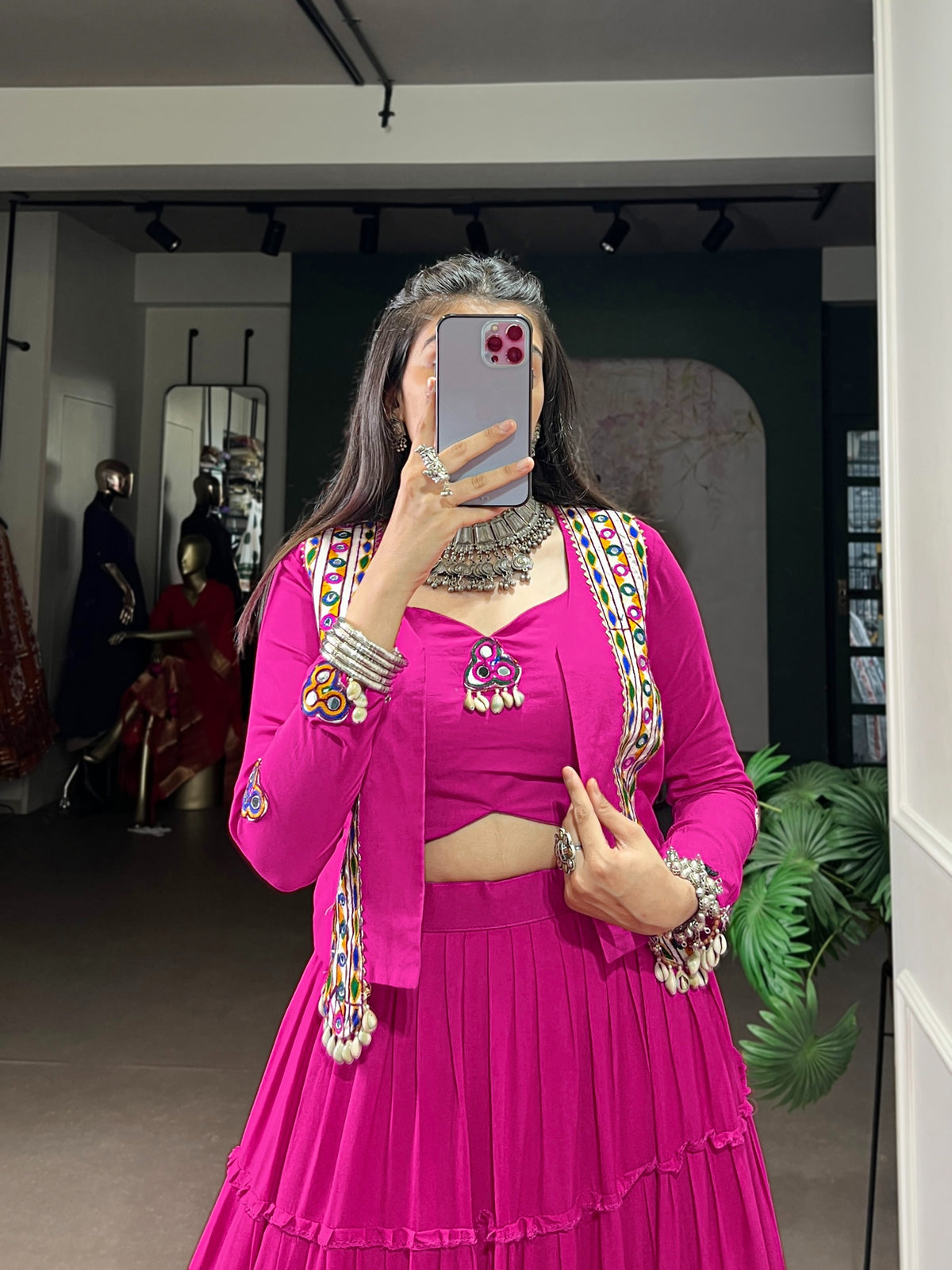 Flat lay front view of rani pink Rajudi Kutchi jacket showing Gamthi embroidery panels, multicolour mirror work and cowrie shell tassels on lapels