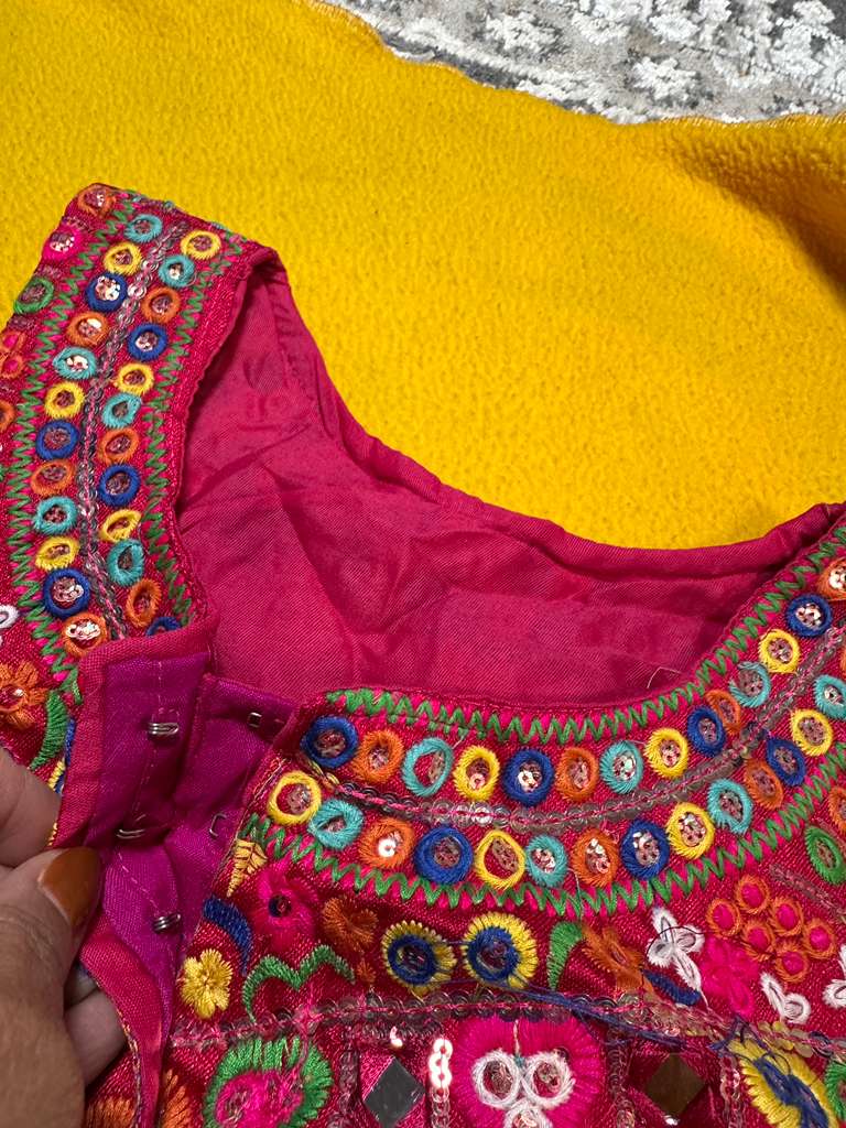 Close-up of magenta Kutchi halter blouse neckline showing hook closure and multicolour Rabari embroidery detail