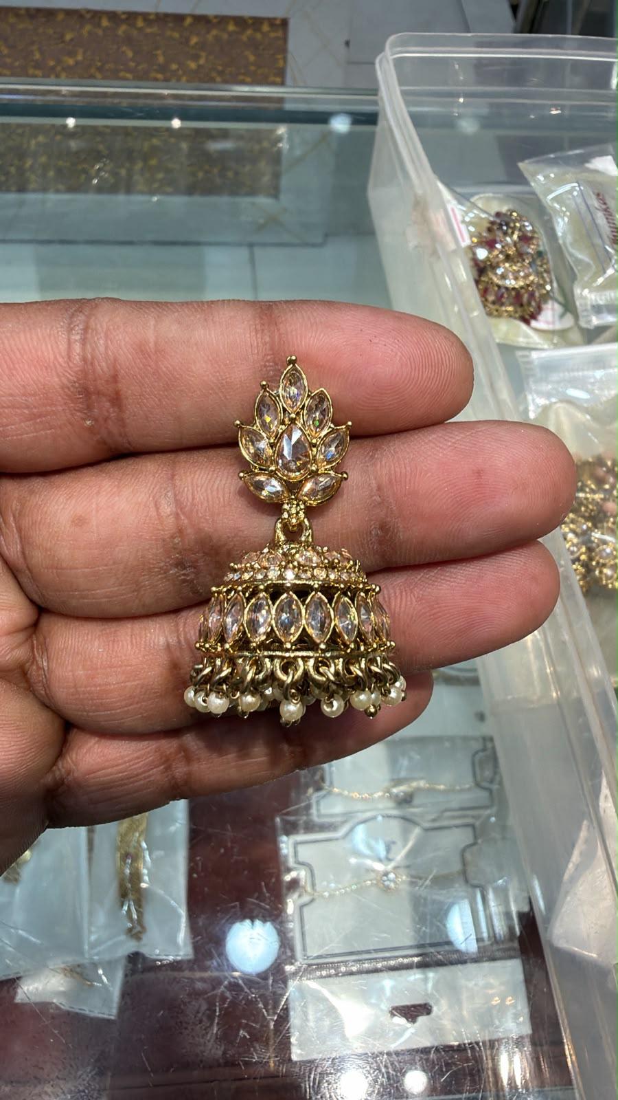Gold jhumka earring held in hand showing lotus fan-shaped marquise CZ stud top and open cage dome body with large marquise CZ stones and faux pearl drops