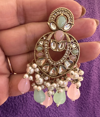 Pastel chandbali earring held in hand showing antique gold crescent frame with mint green, blush pink and lavender polki-look stones, CZ pavé and pearl cluster with pastel bead drops